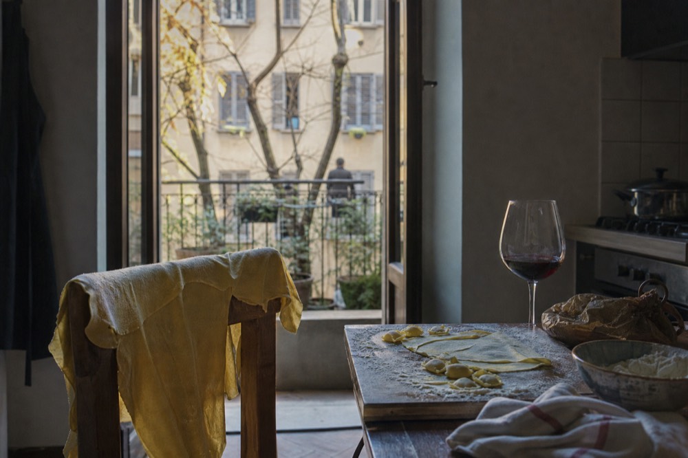 A home kitchen table with rolled fresh pasta and a glass of red wine