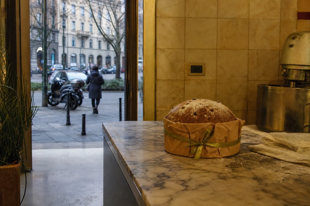 An artisan panettone wrapped in brown paper and ribbon on a marble counter in a Milan pastry shop