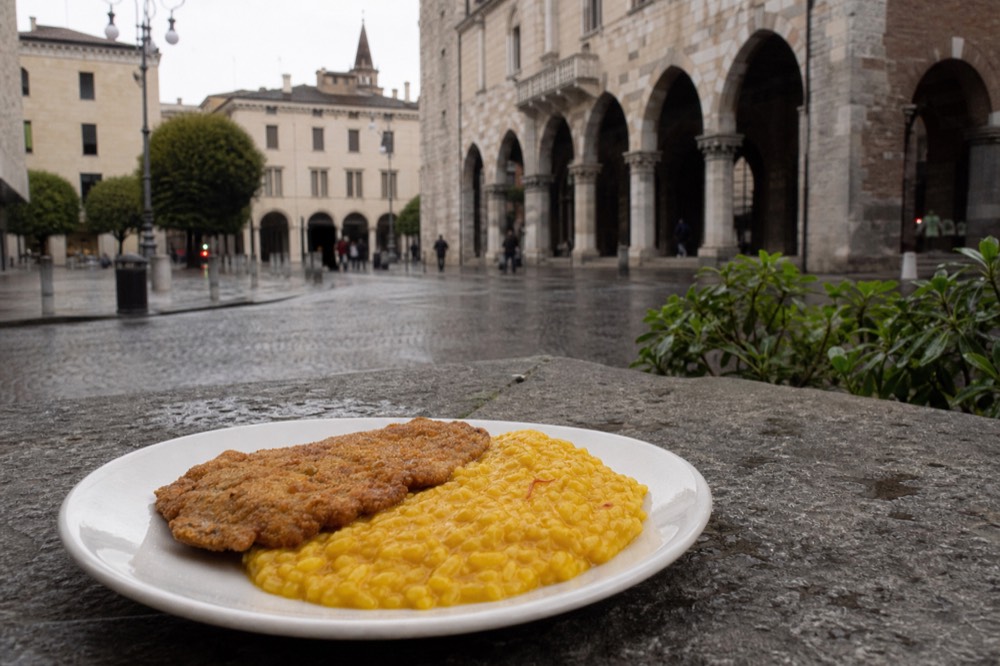 A plate of golden saffron risotto with a breaded veal cutlet on a simple ceramic plate