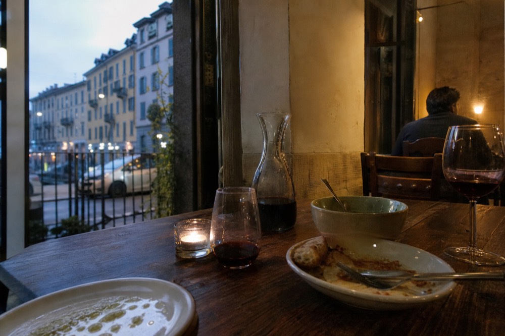 A candlelit dinner table with shared plates and a carafe of wine in a small Milanese dining room