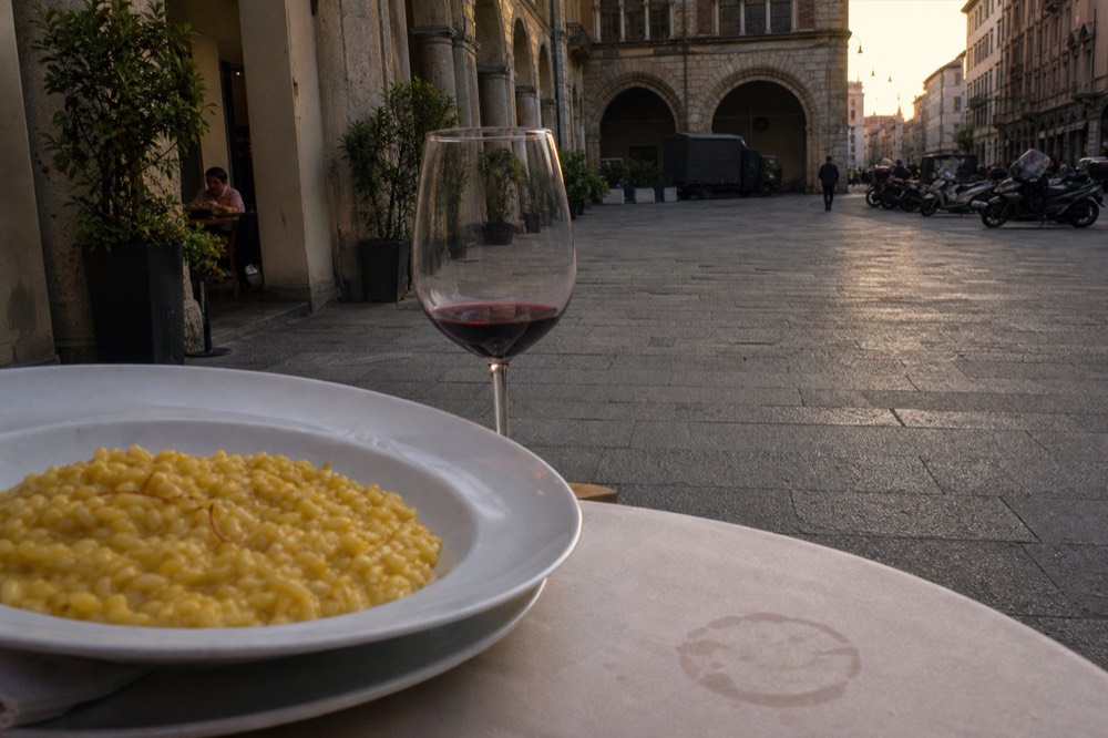 A bowl of saffron risotto with a glass of red wine on a restaurant table
