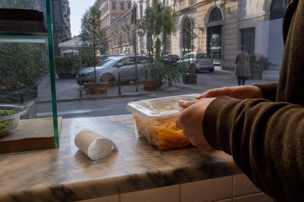 A takeaway container of leftover pasta being closed on a restaurant counter