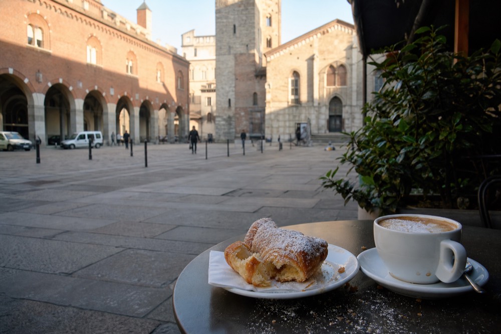 Frothed cappuccino with a cornetto pastry on a small cafe table