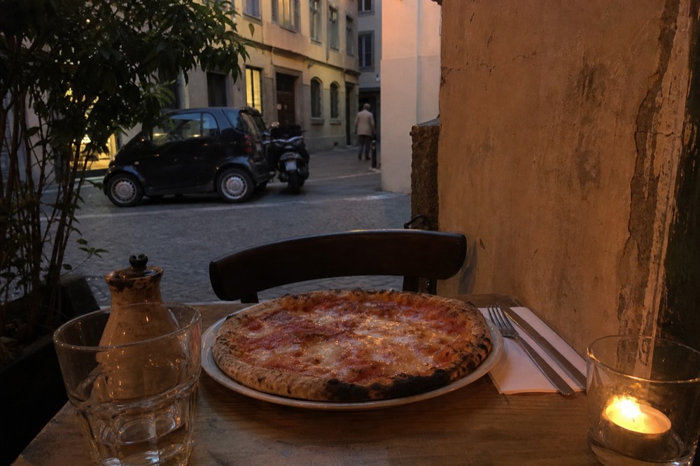 A table set with a knife and fork beside an uncut pizza in a small pizzeria