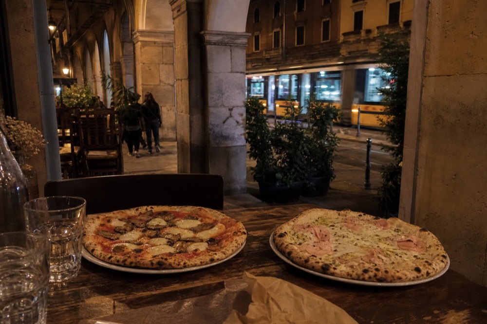 Two whole pizzas served side by side on a rustic table with water glasses