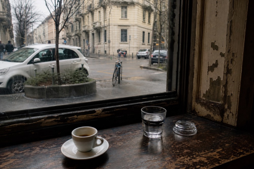 An espresso cup and a glass of water on a dark wooden café counter