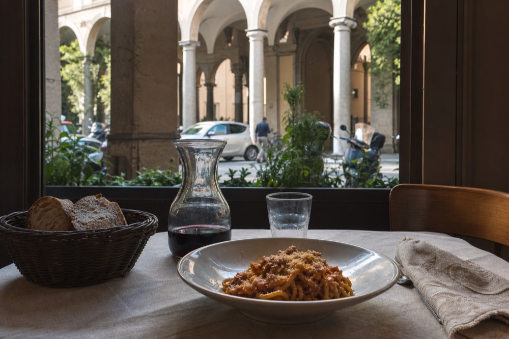 A trattoria table set with a carafe of house wine, bread and a plate of pasta
