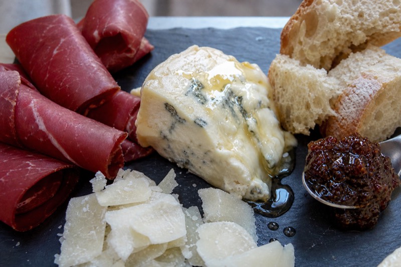 A slate tasting board of rolled bresaola, shaved parmigiano, a wedge of gorgonzola dolce with honey running off it, fig jam and torn country bread