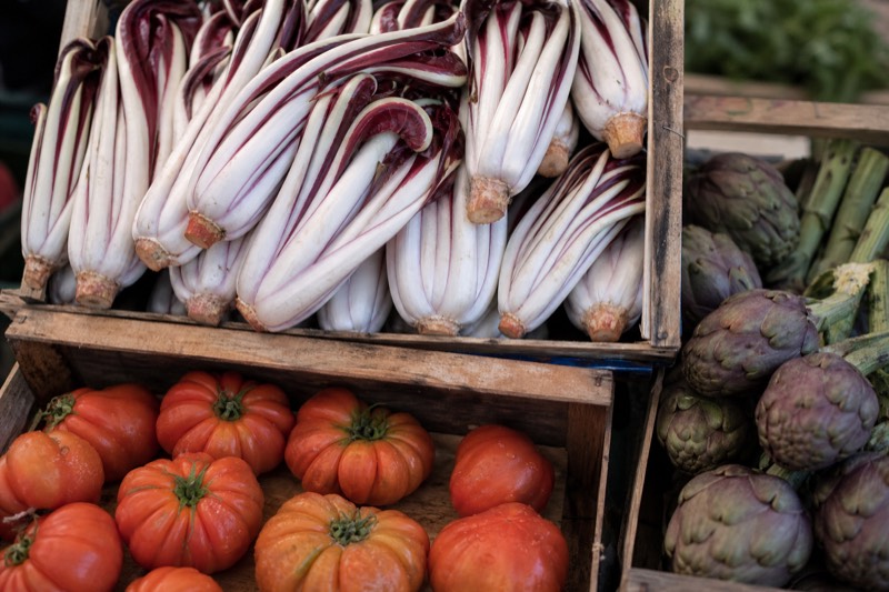Market crates packed with red and white radicchio tardivo, ribbed heirloom tomatoes and violet artichokes