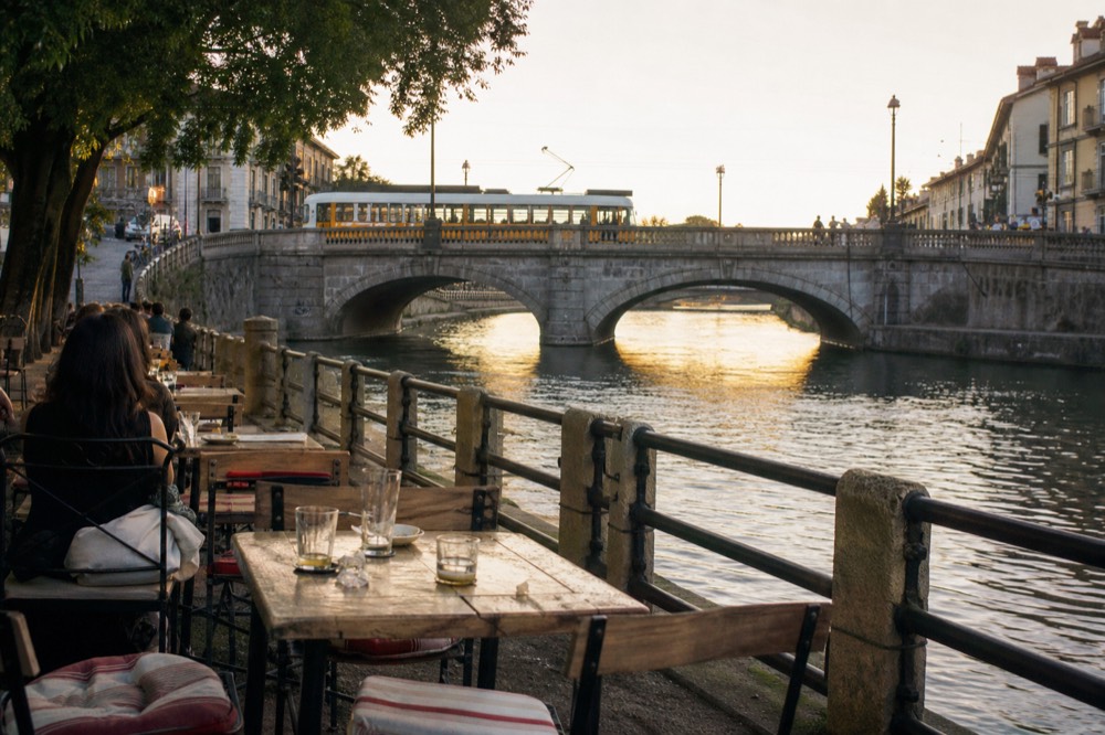 Outdoor aperitivo tables with striped cushions along a Milan canal at golden hour