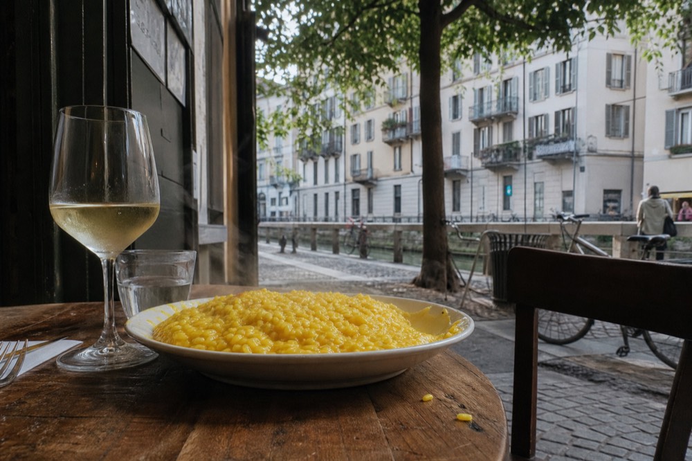 Plate of golden risotto alla milanese beside a glass of white wine