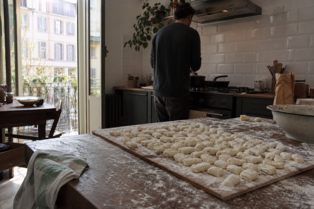 Hands shaping gnocchi dough on a wooden workbench scattered with flour