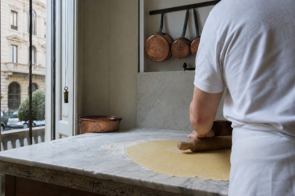 A rolling pin flattening sheets of fresh egg pasta dough on a marble counter
