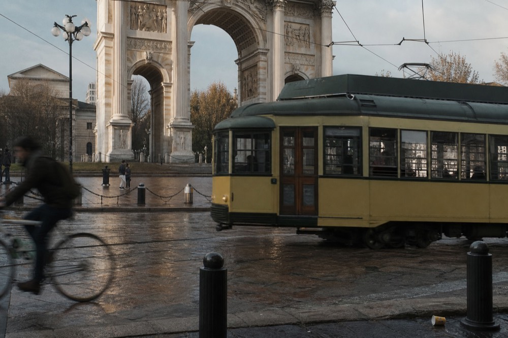 A Milan tram passing a city square with a historic stone building facade in the background