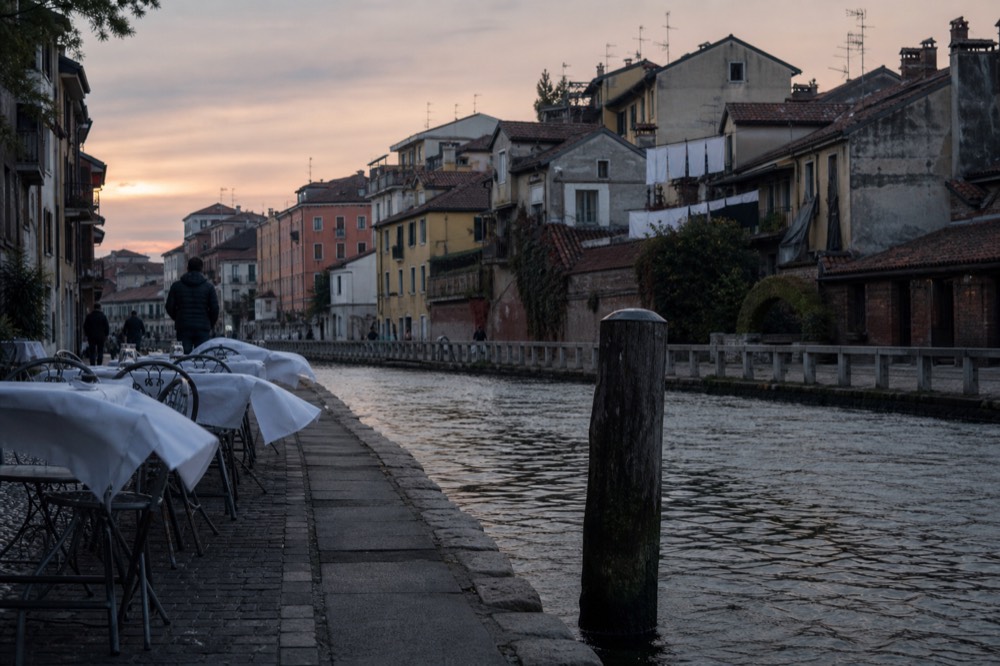 Restaurant tables beside the Naviglio Grande canal at dusk