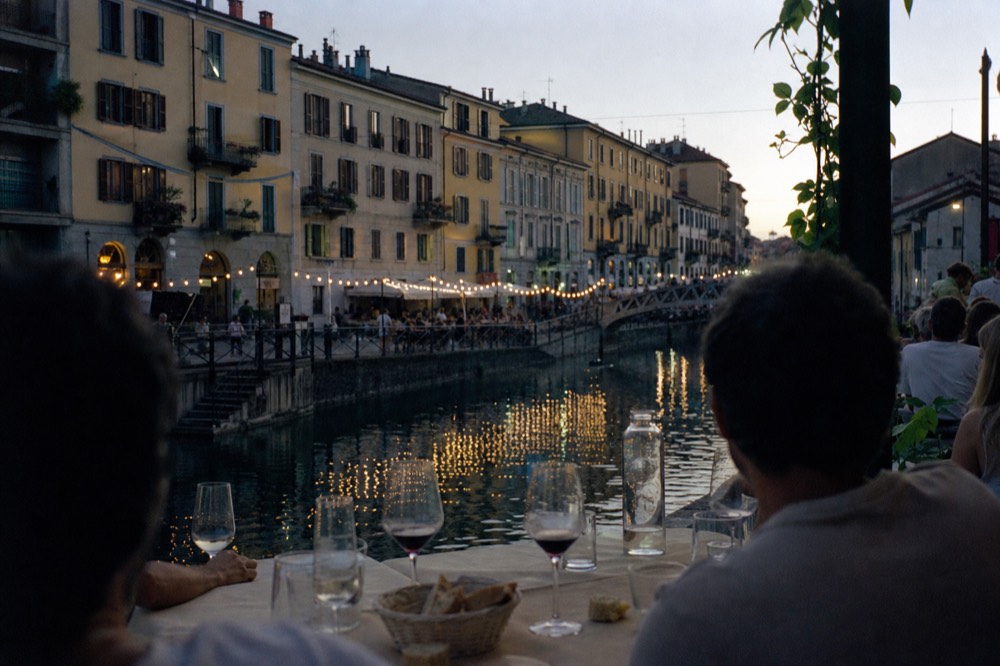 Diners seated at a canal-side restaurant table with wine glasses