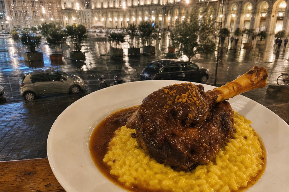 Braised veal shank served on a bed of golden risotto on a white plate