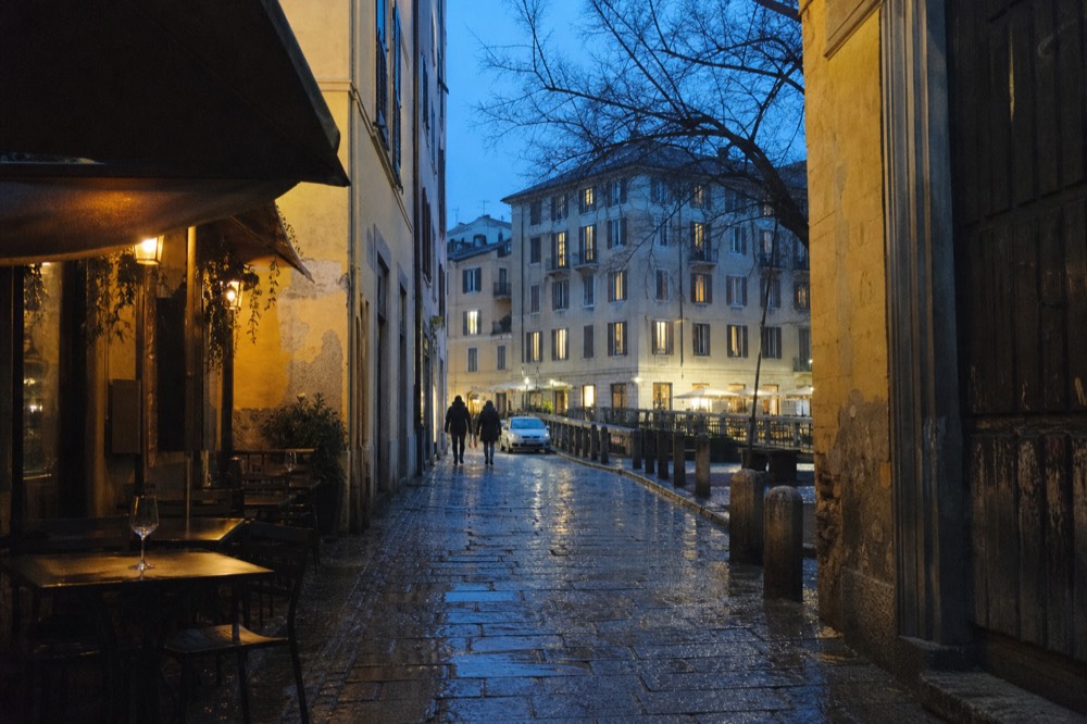 A narrow Milan side street with restaurant awnings and outdoor tables