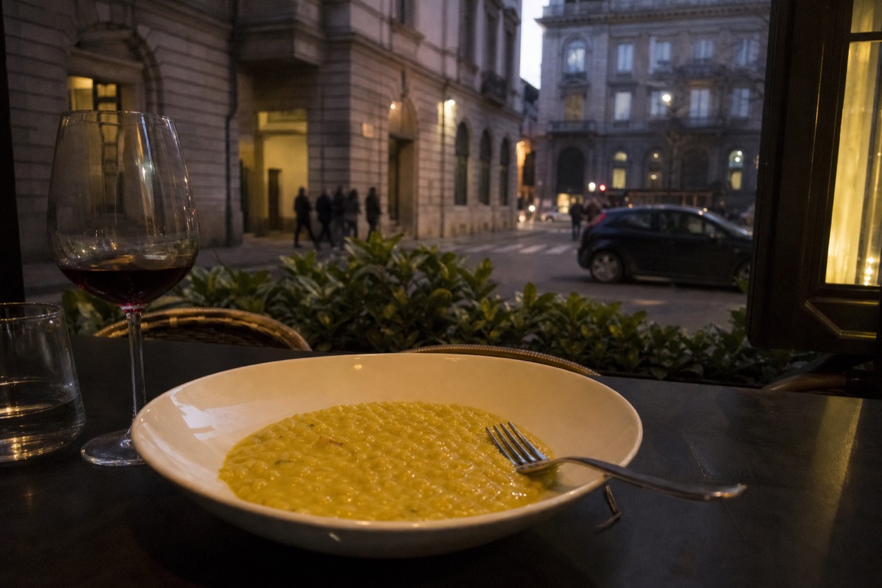 A bowl of golden saffron risotto with a fork resting on the rim at a restaurant table