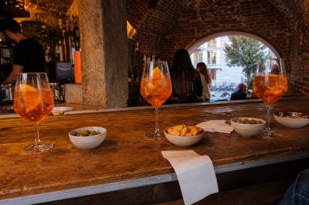 Glasses of orange spritz drinks on a wooden bar counter with snacks